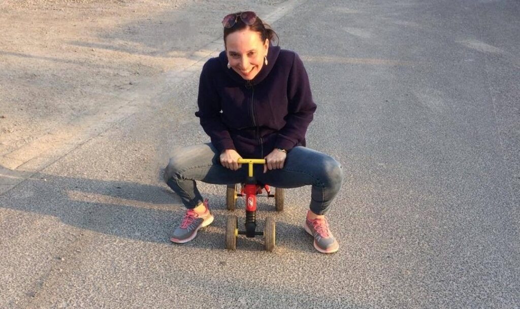 Auf dem Foto sieht man eine Frau Anfang 40, die Dreirad fährt.